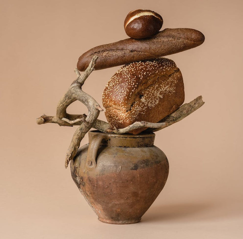 A brown ceramic vase with a stick and 3 breads stacked on top of it