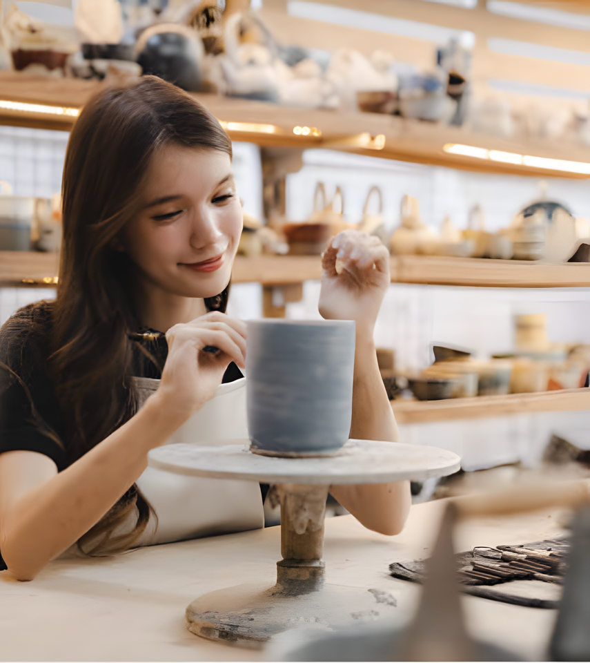 Young cute Japanese woman in ceramic studio smiling whilst painting a large cup