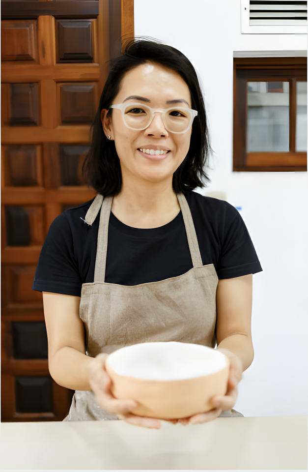 Japanese woman with glasses and in apron holding out a ceramic bowl