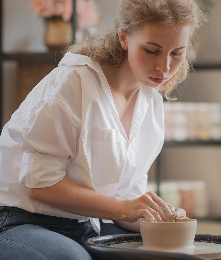 Young woman in ceramics studio shaping a clay bowl