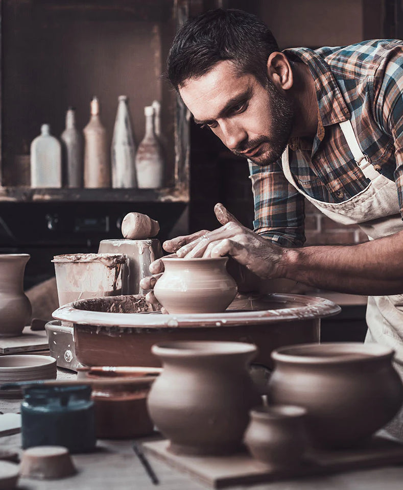 Artistic photo of a man in ceramic studio shaping a small vase on a throwing wheel