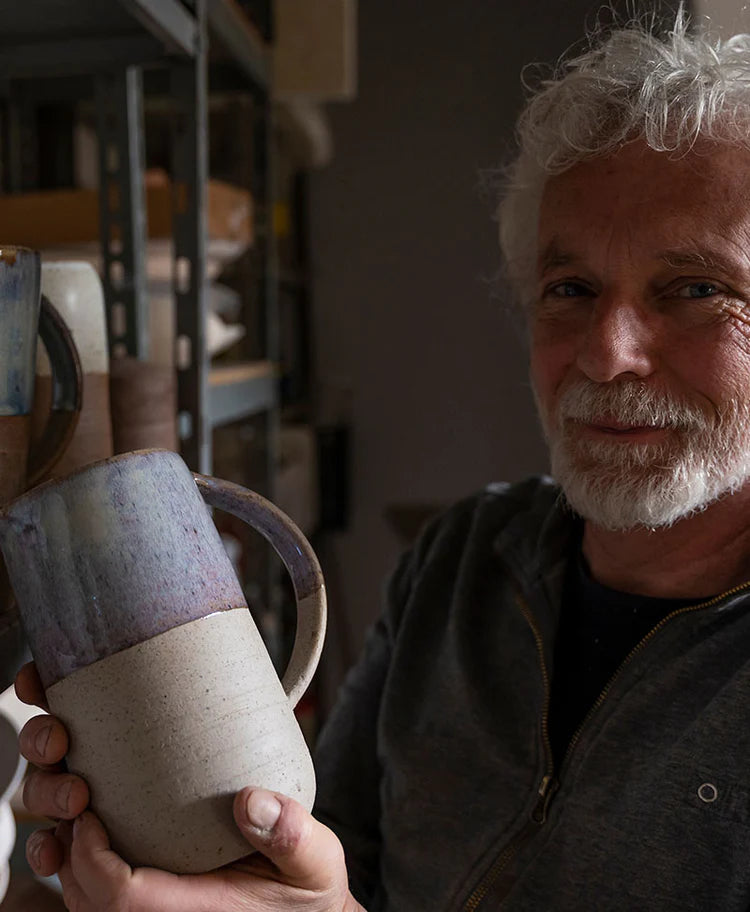 Elderly man with white beard holding up a handmade mug