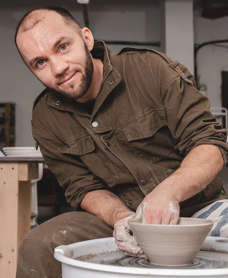 Middleaged man sitting in front of throwing-wheel whilst shaping a clay bowl